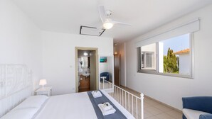 Una habitación de hotel moderna con una cama grande, ventilador de techo, vistas al exterior y un baño con ducha y lavamanos.