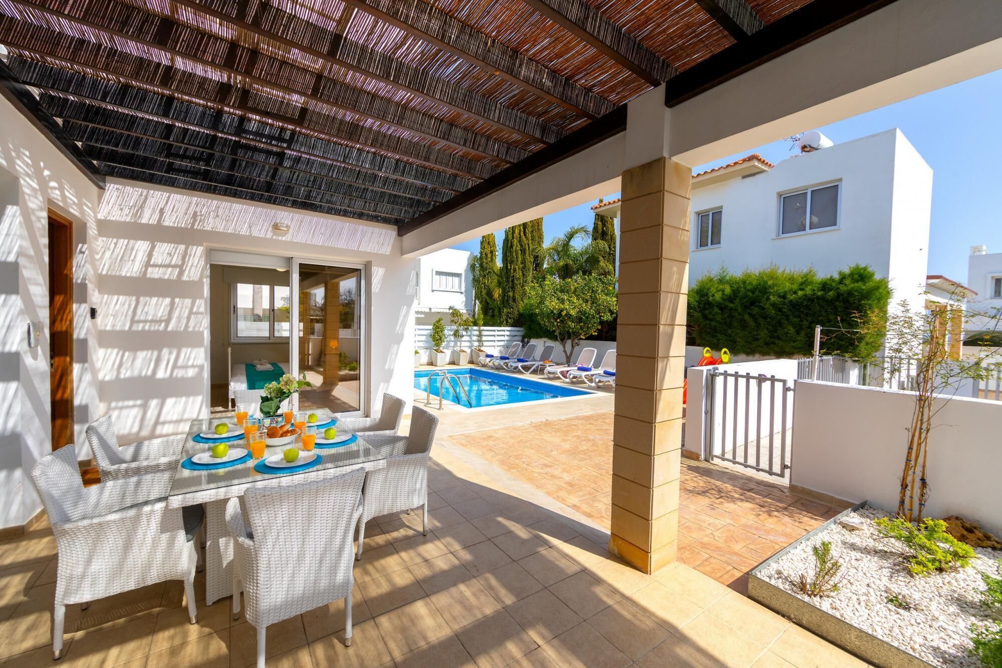 A covered outdoor area with a pool, lounge chairs, and a dining table with breakfast.