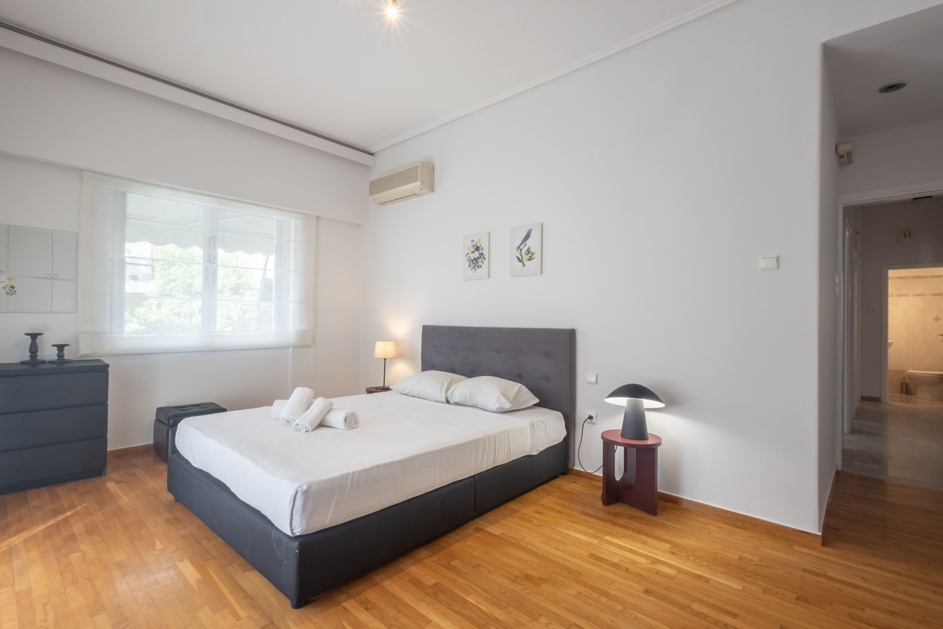 Une chambre à coucher moderne avec un grand lit, une commode, une table de chevet et une fenêtre.