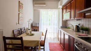 Une cuisine avec des meubles de rangement en bois, une table à manger avec des chaises et une fenêtre ornée de rideaux légers.