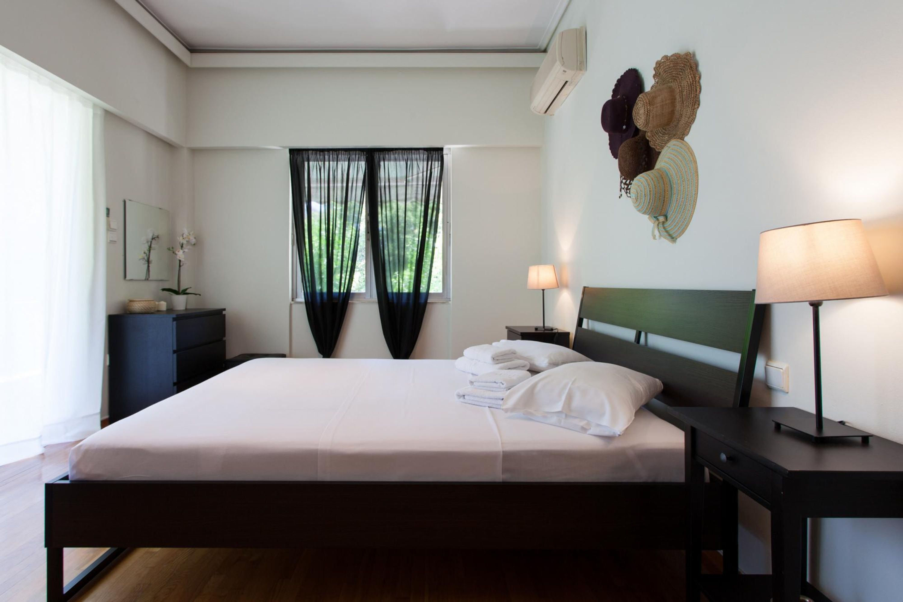 Un lit bien fait, avec du linge de lit blanc et une tête de lit, une table de chevet avec une lampe et un climatiseur fixé au mur.