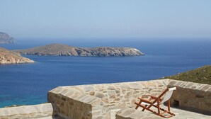 A stone wall with a wooden chair and a white cushion, overlooking a calm sea and rocky terrain. - Spacious 6 Bdrm Stone Villa With Pool (Serifos)