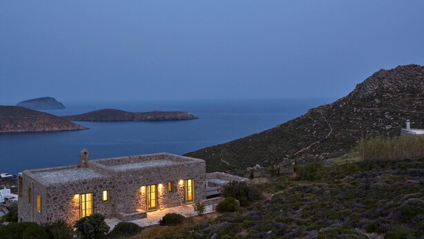 A stone building with a stone roof, surrounded by vegetation and overlooking a body of water. - Spacious 6 Bdrm Stone Villa With Pool (Serifos)