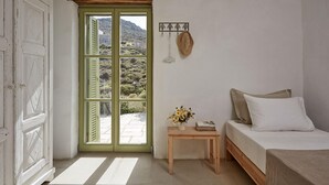 A bedroom with a bed, a small wooden table with a vase of flowers, a green door, and a view of a mountainous landscape. - Spacious 6 Bdrm Stone Villa With Pool (Serifos)