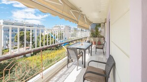 A balcony with a table and chairs, a view of buildings, and a playground in the background. - Luxury and Spacious apt for 8 Guests New Features April 2025 (Alimos)