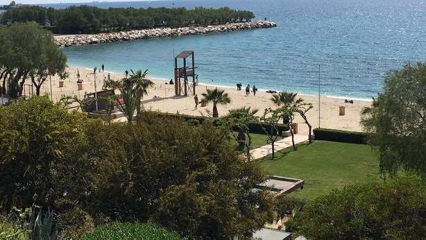A beach with a lifeguard tower, sandy shore, and a rocky breakwater. - Luxury and Spacious apt for 8 Guests New Features April 2025 (Alimos)
