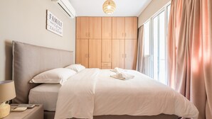 A bedroom with a bed, a nightstand, a lamp, a wall-mounted air conditioner, a ceiling light, and a window with curtains. - Luxury and Spacious apt for 8 Guests New Features April 2025 (Alimos)