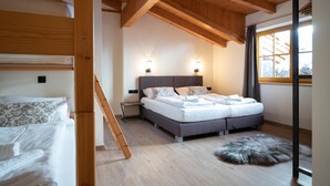 Une chambre avec un plafond en bois, un lit doté d’une tête de lit grise, deux tables de chevet avec des lampes et une grande fenêtre avec des rideaux.
