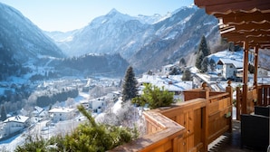 Un paysage montagneux avec des bâtiments enneigés et une terrasse en bois donnant sur une vallée.