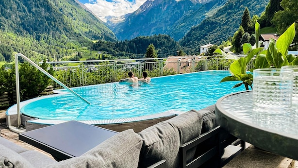 Une piscine où se trouvent deux personnes, entourée de montagnes et de verdure.