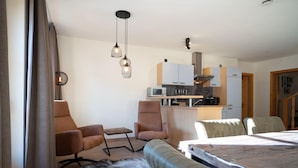Une chambre d’hôtel moderne comprenant un canapé, deux fauteuils, un tapis en fourrure, un lit, une kitchenette et un coin repas.
