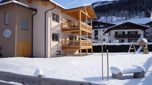 A multi-story building with a wooden balcony, snow-covered ground, and mountains in the background. - Tauern Relax Lodges - Penthouse (Kaprun)