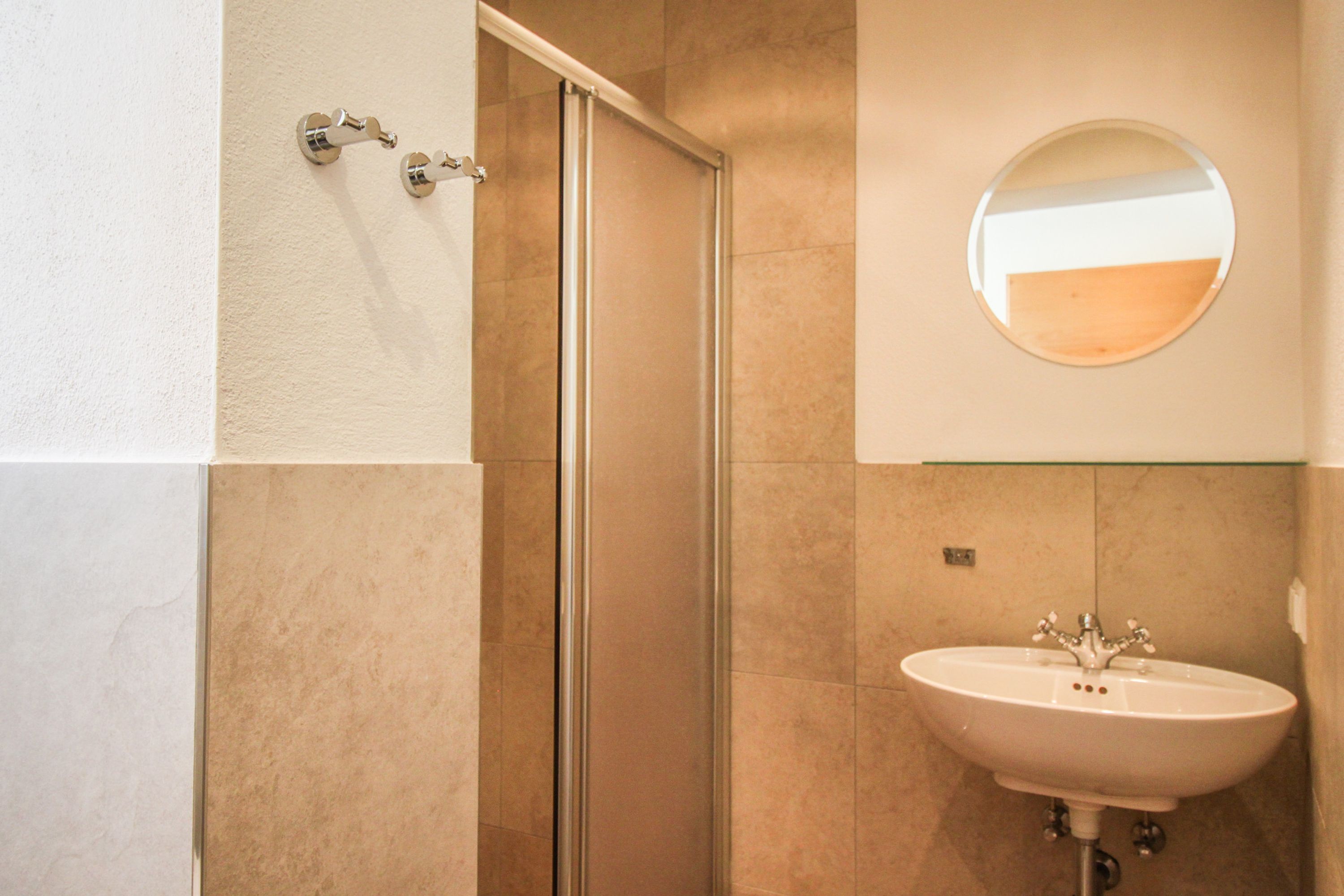 A bathroom with a glass shower door, a sink with a mirror above it, and beige tiled walls.