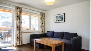 A modern living room with a dark grey sofa, a wooden coffee table, and a large window with patterned curtains. - Tauern Relax Lodges - Penthouse (Kaprun)