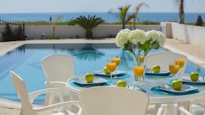 Mobiliario de comedor junto a la piscina con una mesa preparada para dos personas, con vistas al océano.
