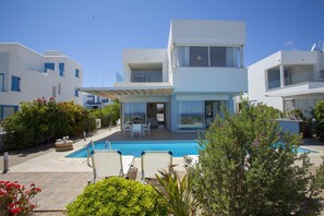 A modern two-story house with a swimming pool, outdoor furniture, and lush greenery. - Villa Melissa Selana (Paralimni)