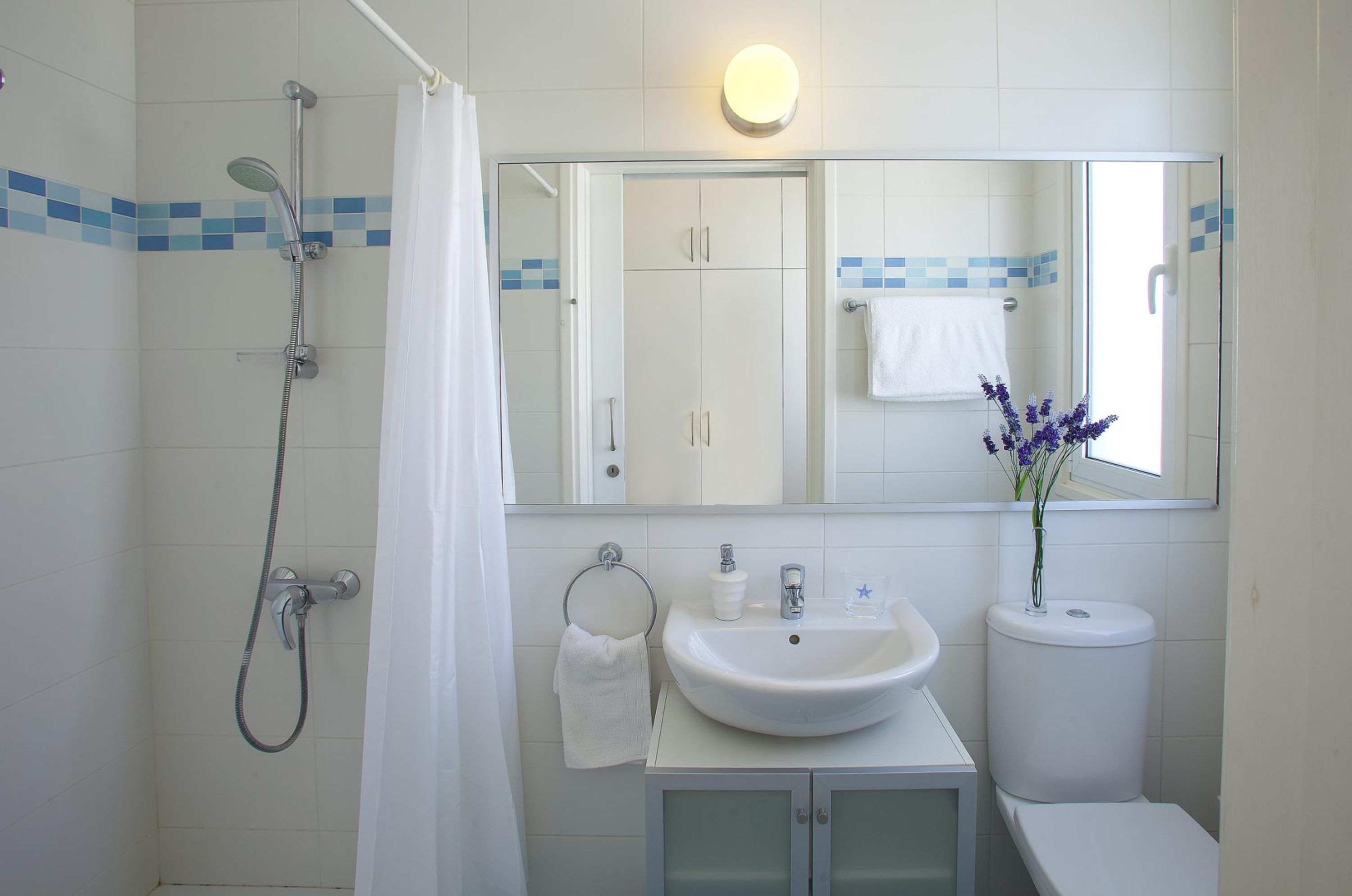 Un baño con ducha, lavabo, inodoro y espejo, con una toalla colgada en la pared.