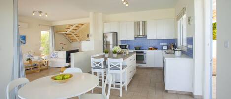 Une cuisine moderne avec des meubles blancs, un coin repas doté d’une table ronde et de chaises, et un escalier menant à un autre niveau.
