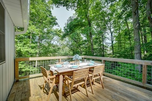 A wooden deck with a table set for four, surrounded by a wooden railing, overlooking a forested area. - Maryland Vacation Rental w/ Private Pool & Dock (Lusby)
