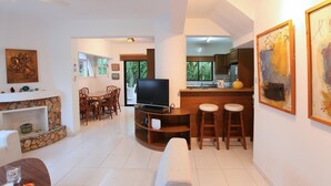 Sala de estar com televisão, móveis de madeira, lareira de pedra e área de cozinha com balcão.