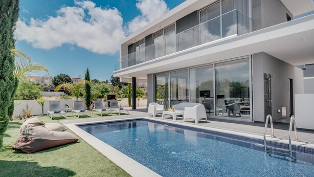 Ein modernes Haus mit Swimmingpool, Sitzgelegenheit im Freien und einer verglasten Terrasse.