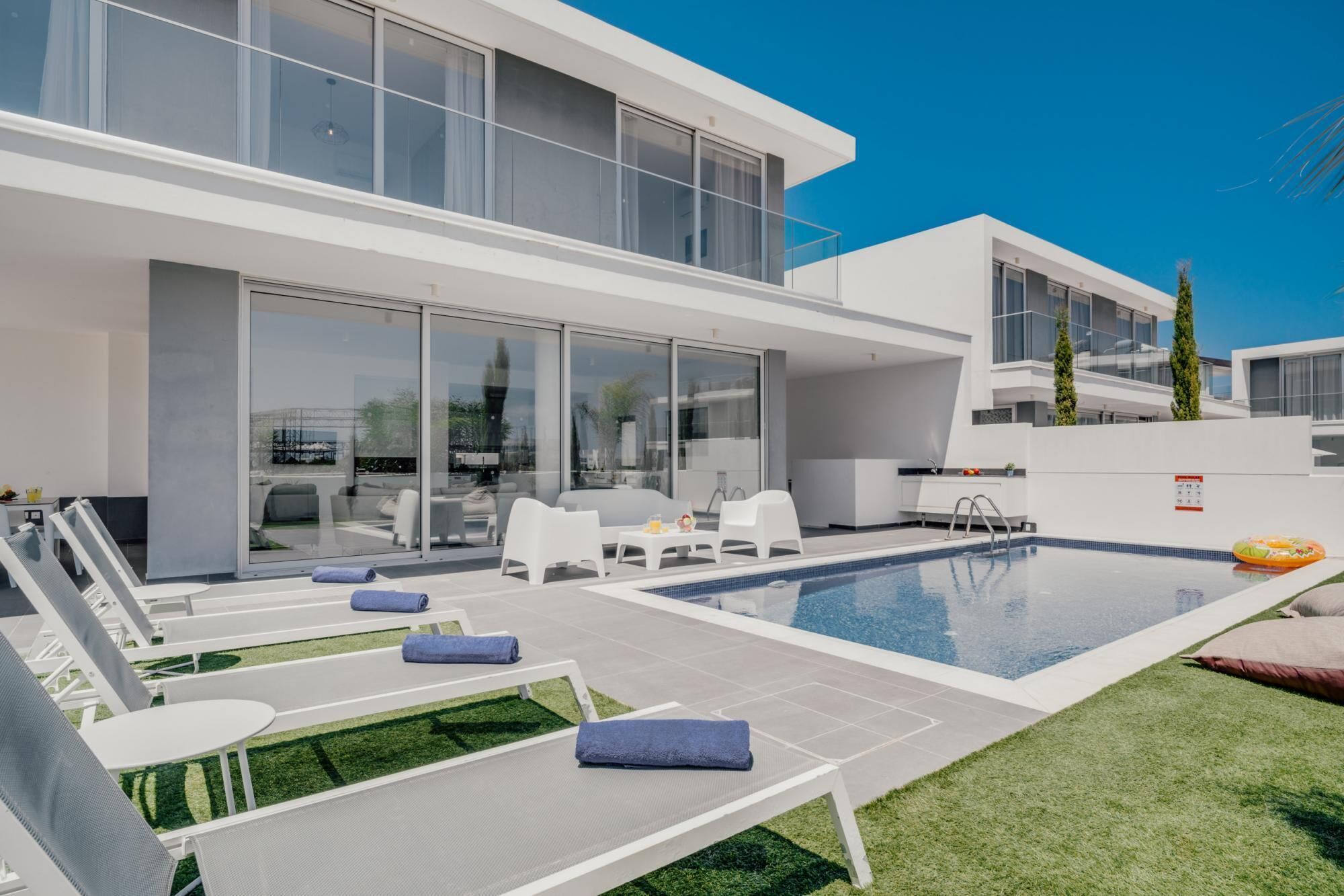 Un espace moderne aménagé au bord de la piscine, avec des chaises longues, une piscine et un patio fermé par des baies vitrées.