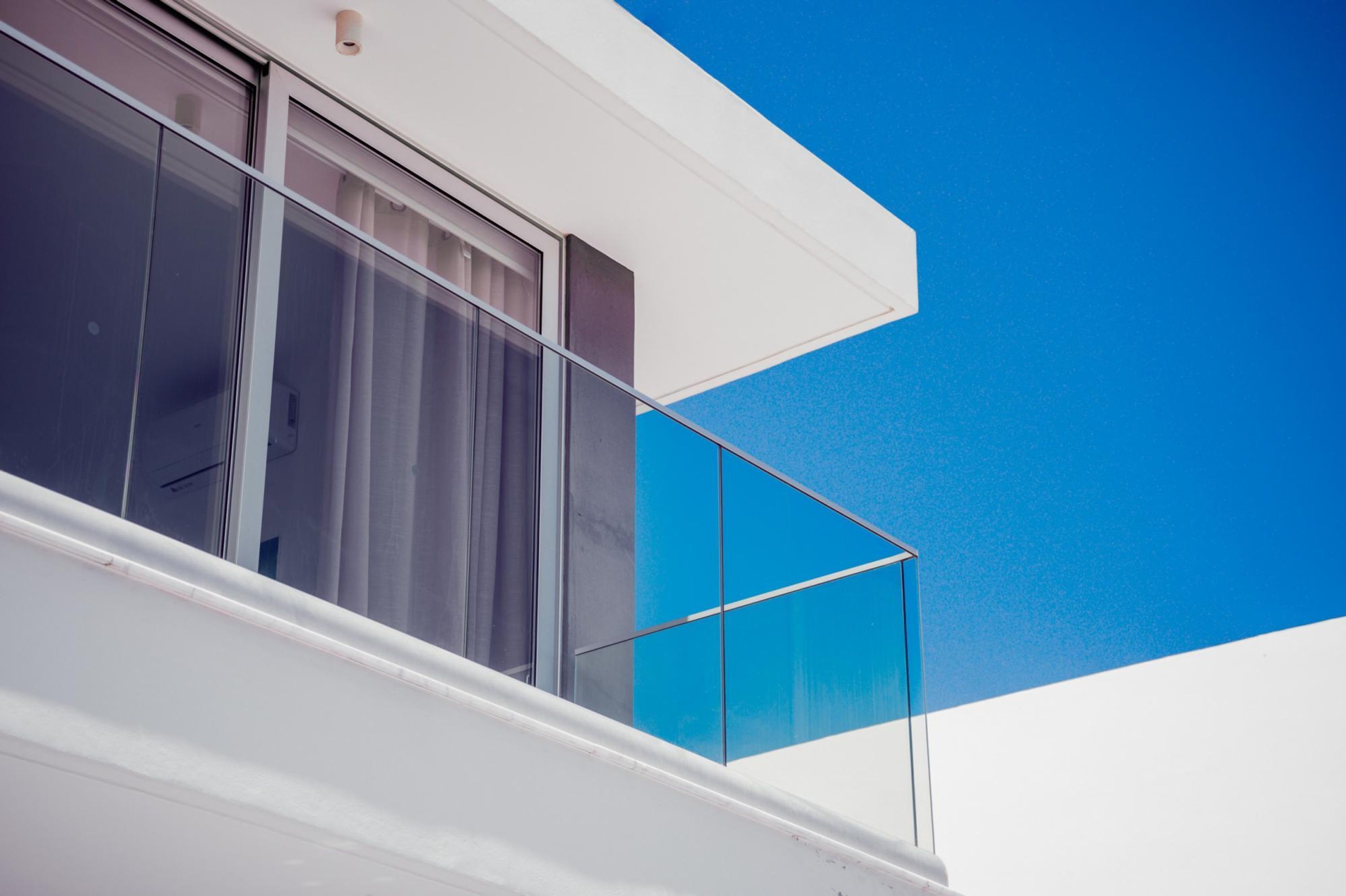 En moderne bygning med store vinduer og en balkon med gelænder af glas.