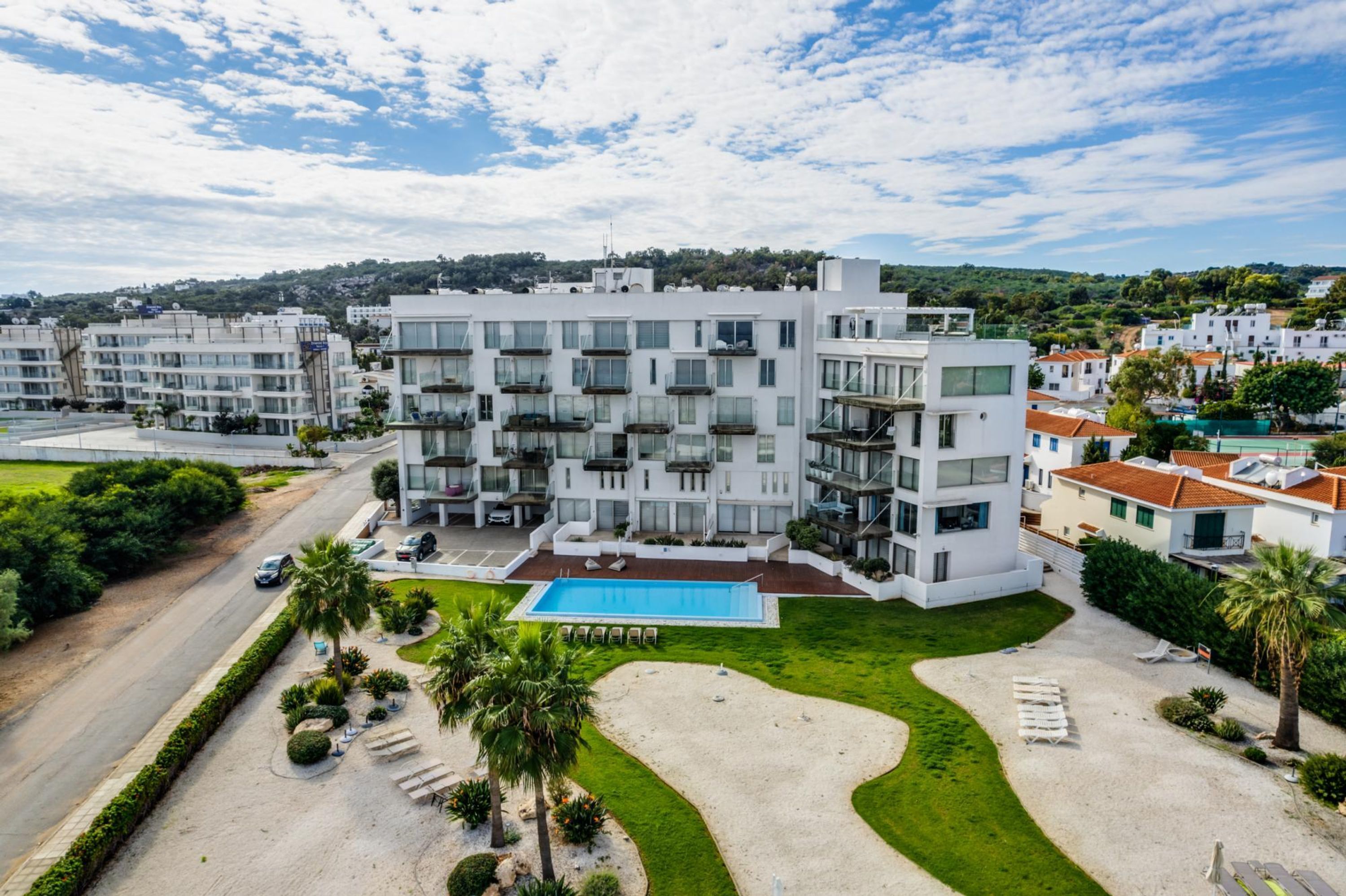 Un hotel moderno de varios pisos con piscina, rodeado de vegetación y un cielo despejado.
