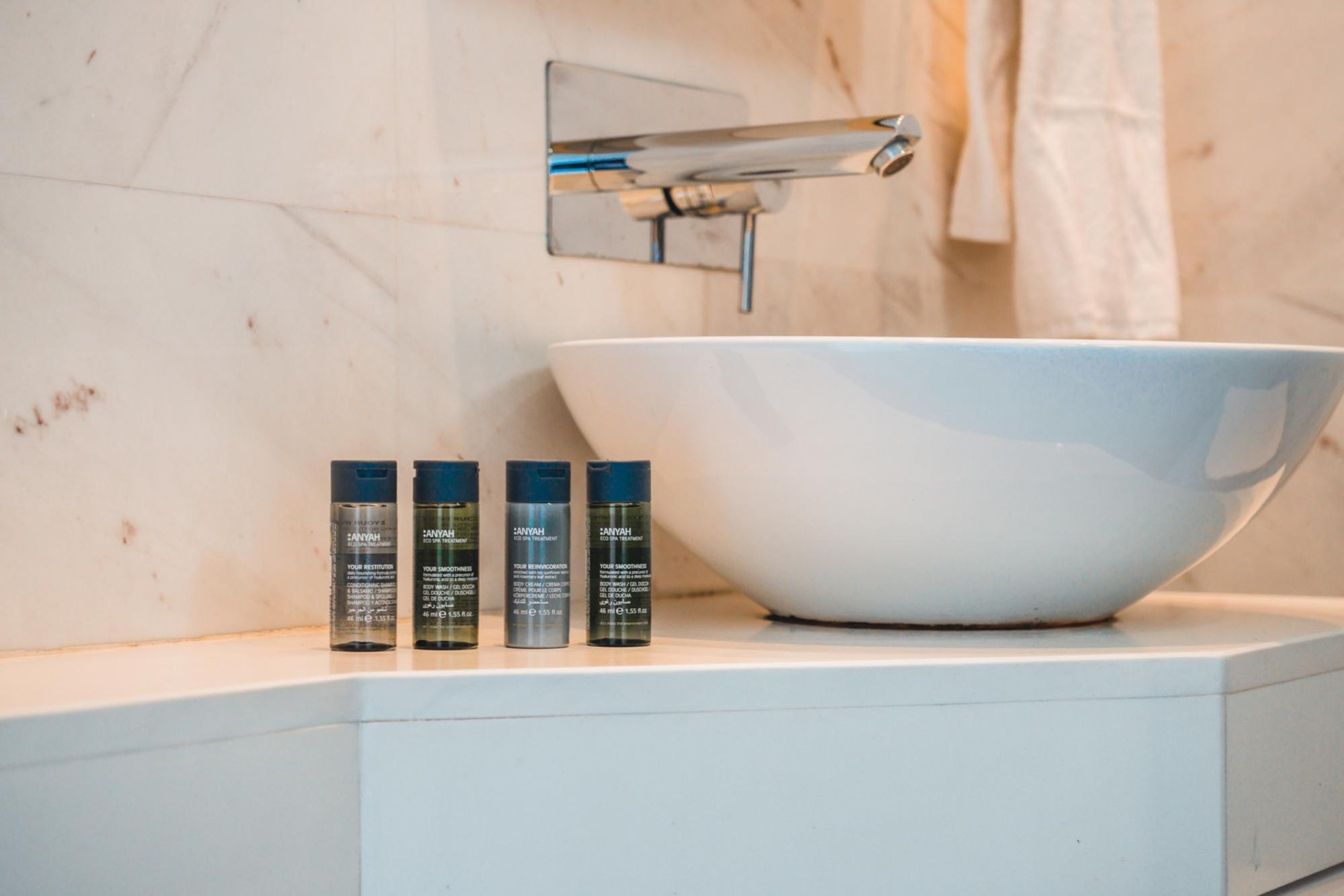 A bathroom with a white sink, three bottles of hair care product, and a towel rack.