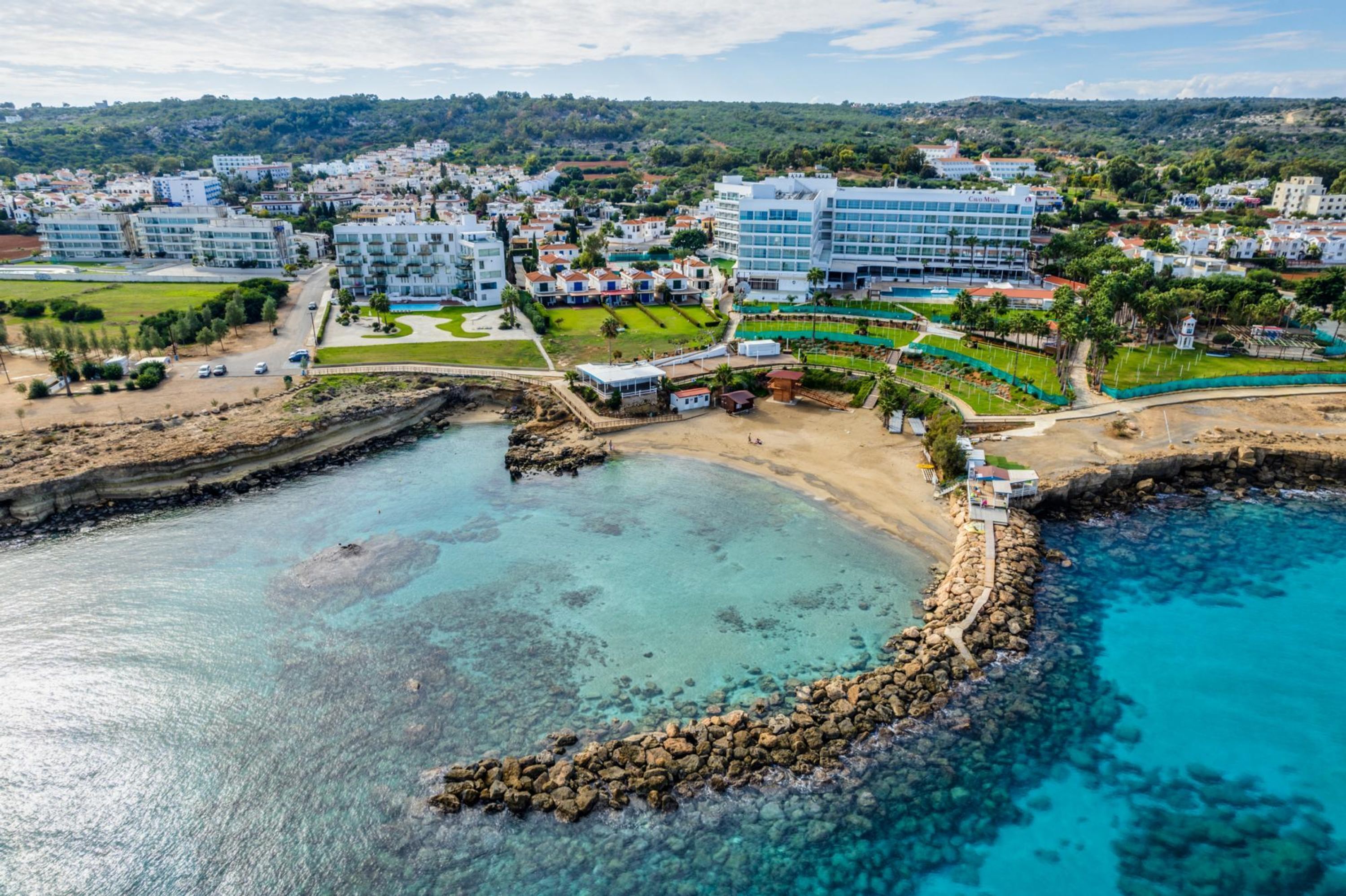 Hotel à beira-mar com costa rochosa, águas azul-claras e vista para a cidade ao redor.