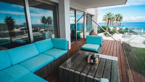 Un balcón con un sofá turquesa y una mesa de centro de vidrio, con vista a una playa con palmeras y el océano.