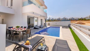 A modern outdoor pool area with a dining setup and lounge chairs. - Protaras Sol e Mar Villa 3 (Paralimni)