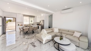 A modern living room with a sectional sofa, a dining area with a table and chairs, and a kitchen in the background. - Protaras Sol e Mar Villa 3 (Paralimni)