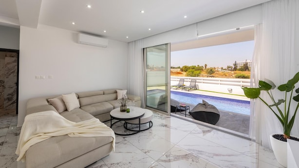 A modern living room with a large sofa, a coffee table, and a view of a swimming pool and outdoor area. - Protaras Sol e Mar Villa 3 (Paralimni)
