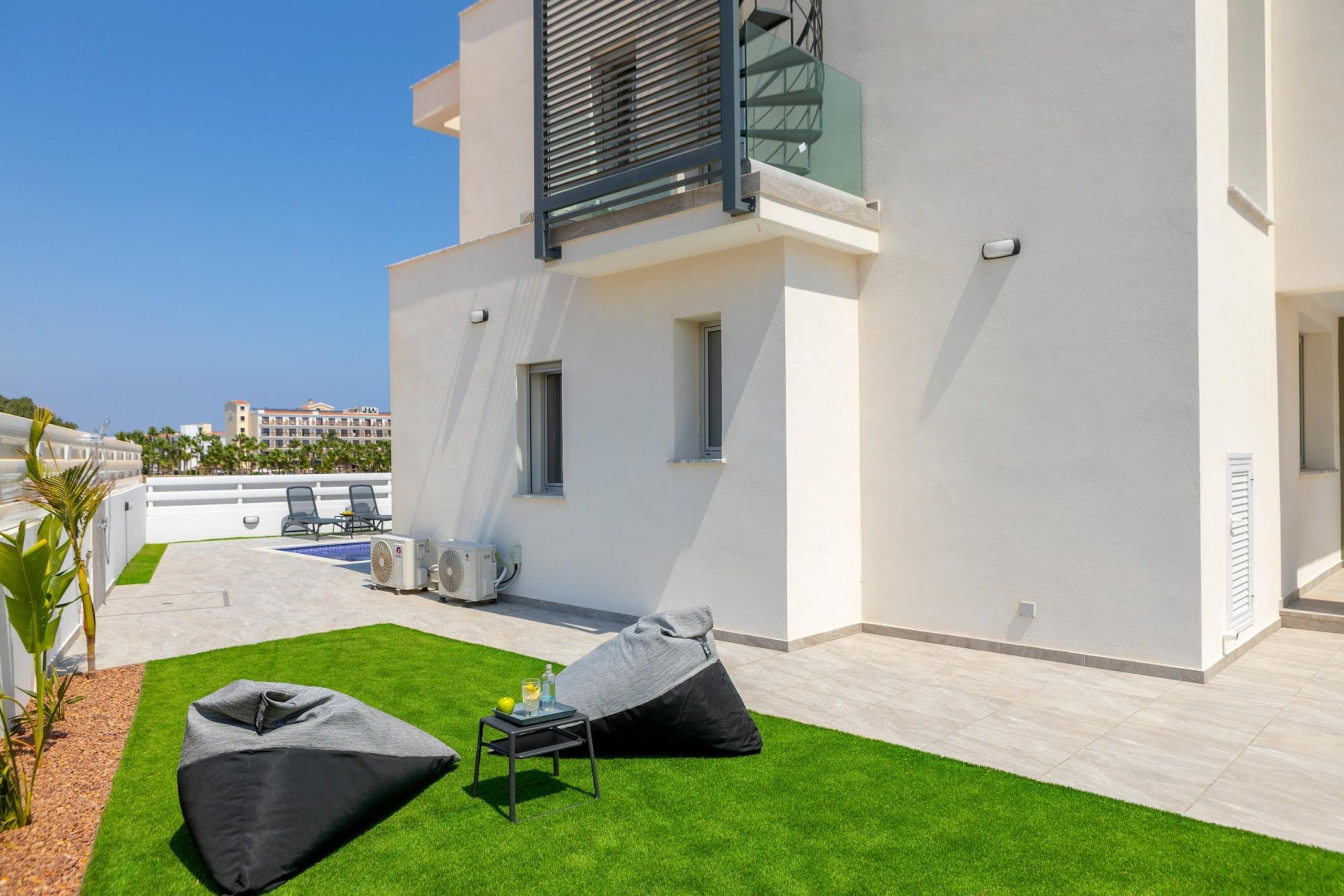 A modern outdoor patio with a pool, two bean bags, and a small table with a drink.