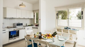 Een moderne keuken met witte kasten, een magnetron en een ontbijtgedeekte eethoek met een glazen tafel.