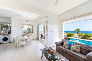 A modern living room with a view of the sea, a dining area, and a kitchen with a washing machine. - Protaras Artisan Seafront Villa 1 (Paralimni)