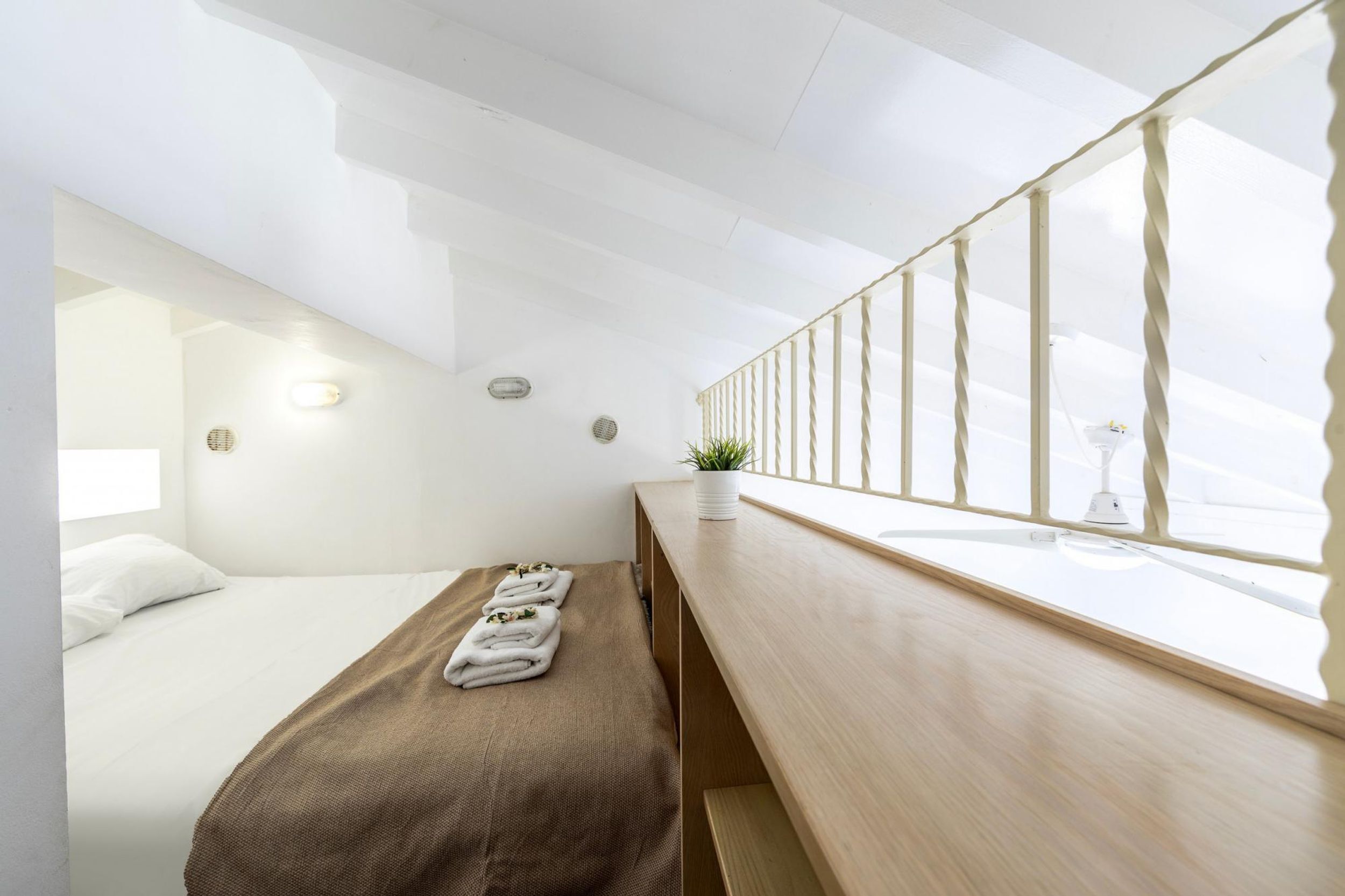 A modern hotel room with a bed, a bench, a small table with a plant, and a window with a view.