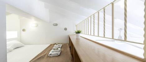 A modern hotel room with a bed, a bench, a small table with a plant, and a window with a view.