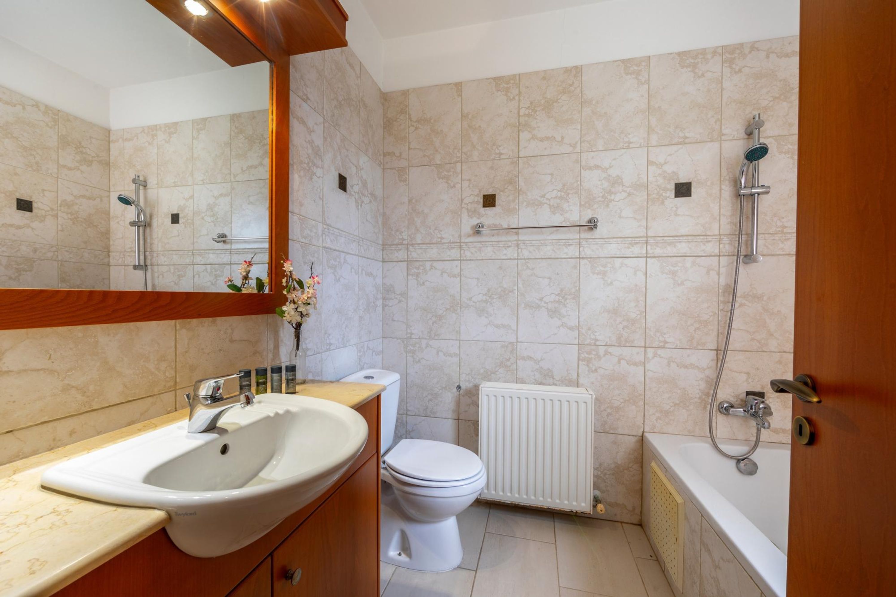 Et badeværelse med vask, toilet, bruser og et spejl.
