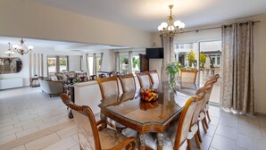 A spacious dining area with a large wooden table surrounded by upholstered chairs, a chandelier, and a large mirror. - Protaras Posidon By The Sea (Paralimni)