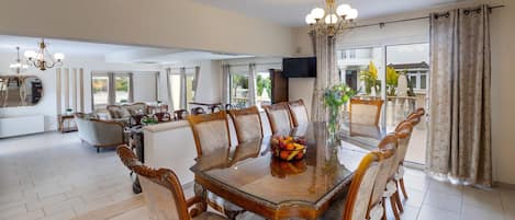 A spacious dining area with a large wooden table surrounded by upholstered chairs, a chandelier, and a large mirror.