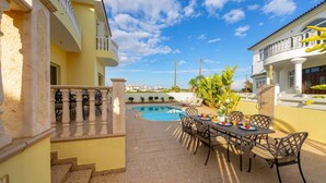 A poolside area with a dining table and chairs, a staircase, and a view of the pool and surrounding buildings. - Protaras Posidon By The Sea (Paralimni)