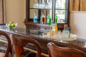 A dining table with a glass bowl of apples, a bottle of orange juice, and various bottles and glasses. - Protaras Posidon By The Sea (Paralimni)