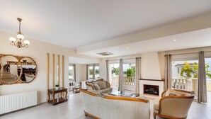 A spacious living room with a large sofa, a fireplace, and a view of the outdoors. - Protaras Posidon By The Sea (Paralimni)