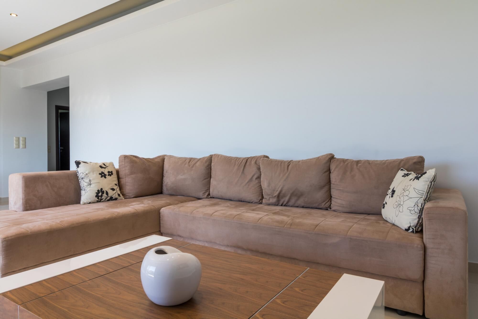 A modern living room with a large L-shaped sectional sofa, a white vase, and a wooden coffee table.