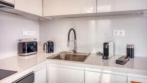 A modern kitchen with white cabinets, a stainless steel sink, a kettle, a toaster, and a coffee maker. - Lux Deck Roof Apt at the Foothills of Acropolis w Breathtaking View (Athens)