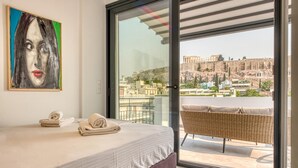 A hotel room with a bed, a painting, a view of a cityscape, and a balcony with wicker furniture. - Lux Deck Roof Apt at the Foothills of Acropolis w Breathtaking View (Athens)