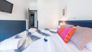 A hotel room with a bed, a bedside table with a lamp, a wall-mounted TV, and a door leading to another room. - New Relaxed Central Apartment Walk Everywhere (Athens)