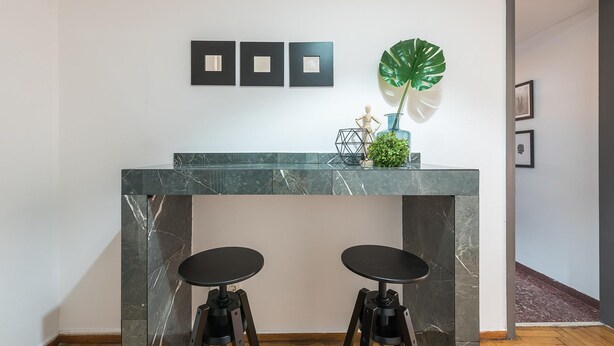 A modern kitchen with a marble countertop, two stools, and decorative items including a large green leaf and framed pictures. - New Relaxed Central Apartment Walk Everywhere (Athens)